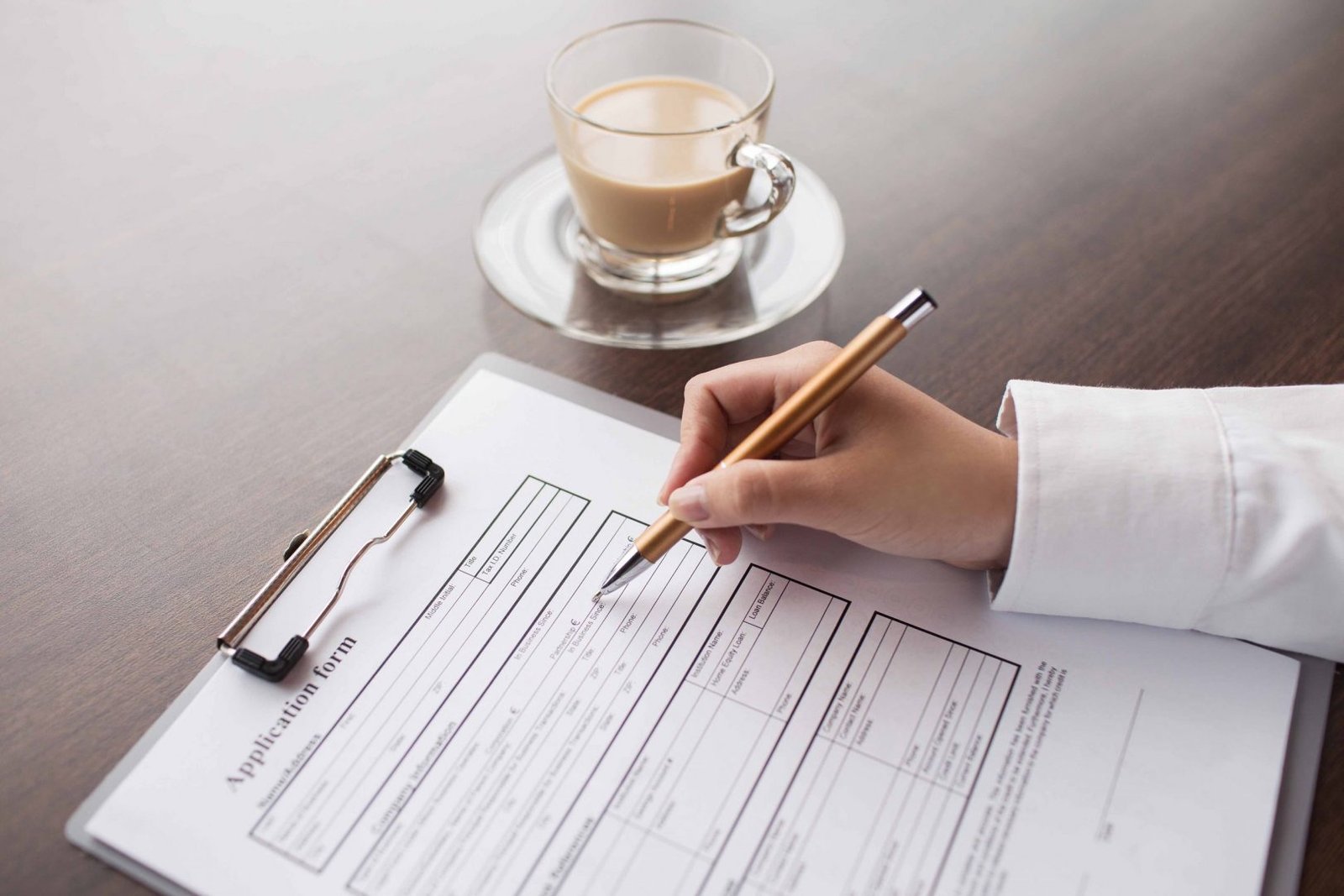 Hand of female candidate writing down information in application form, coffee cup in table
