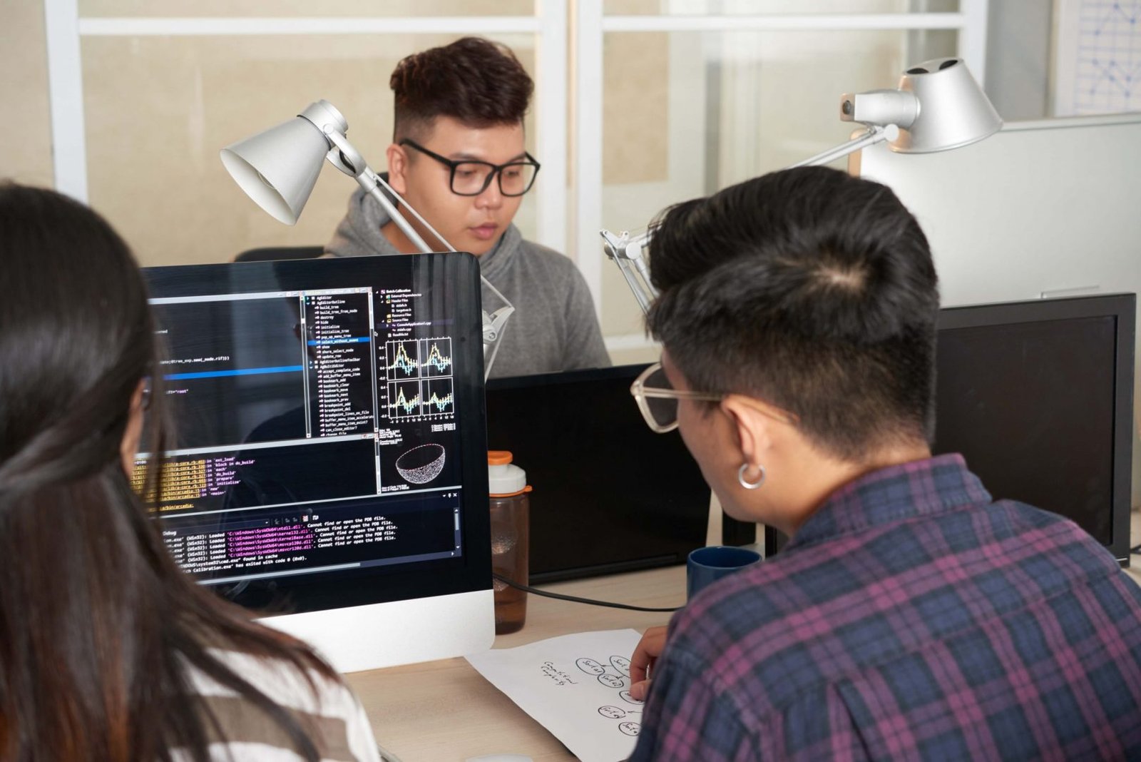 Back view of male and female programmers working together on ambitious project while sitting at spacious open plan office